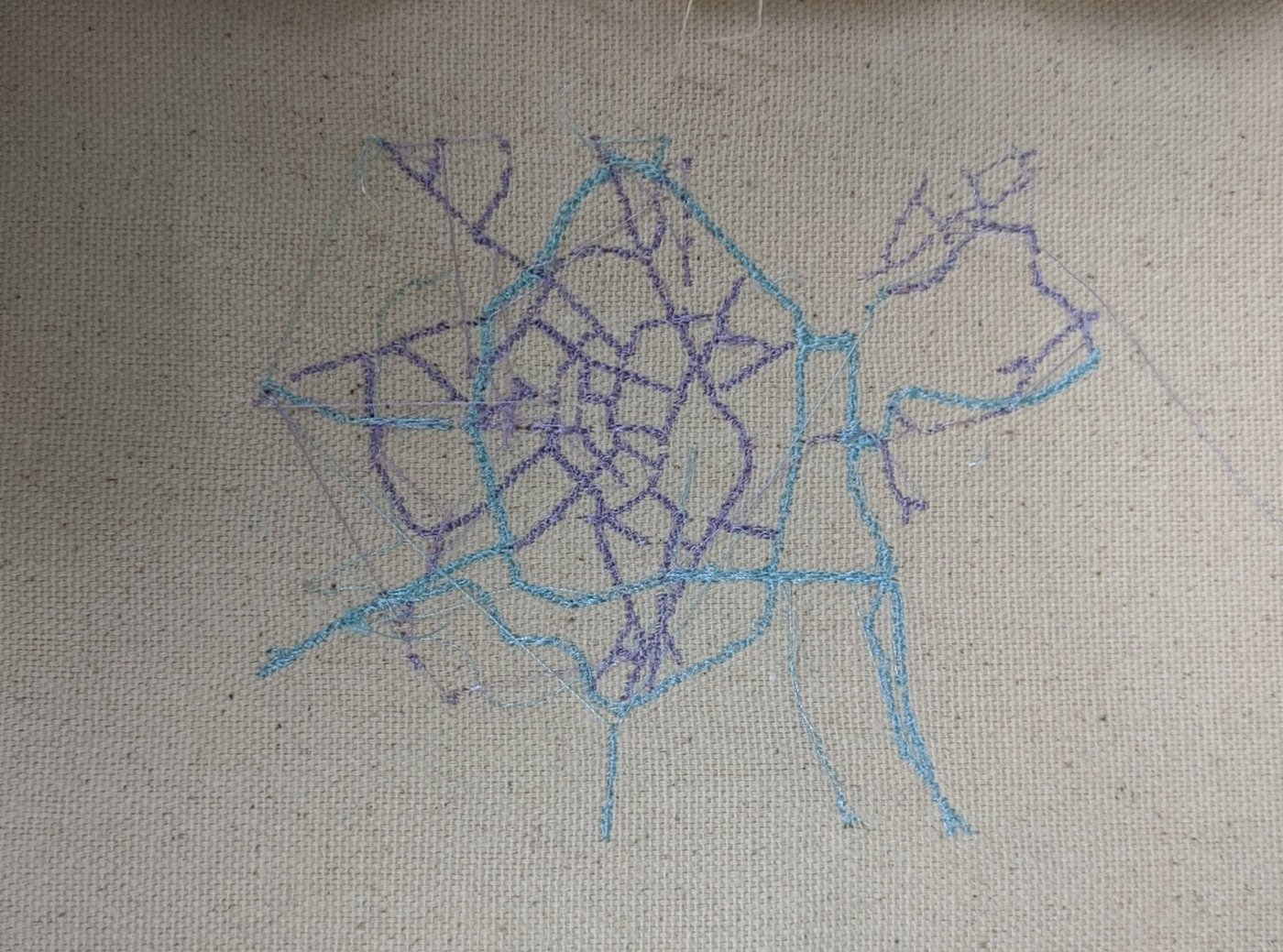 A city street map embroidered in purple and teal thread on natural canvas