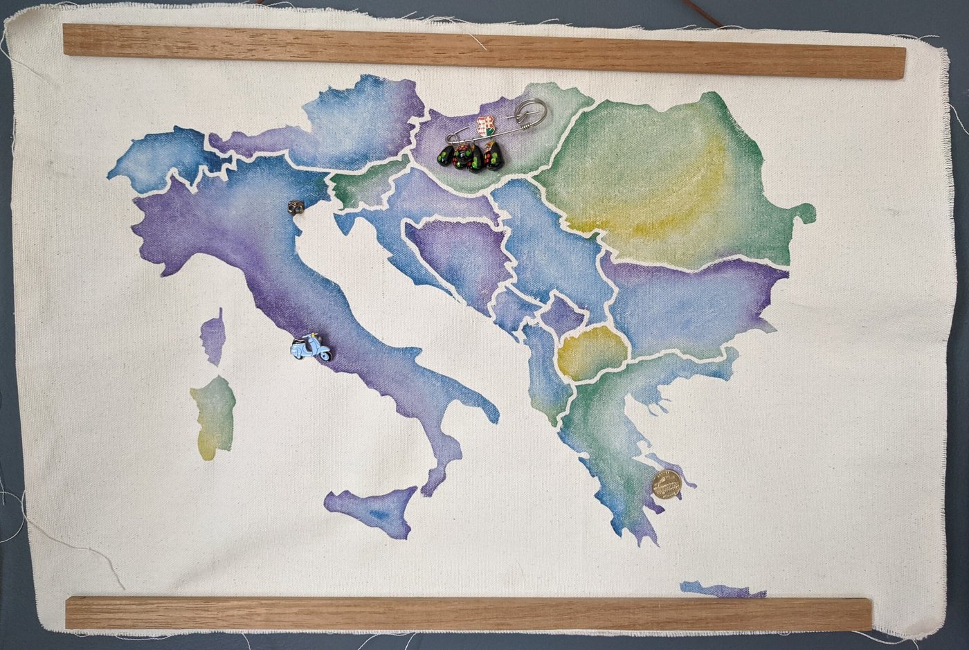 Watercolor map of central Europe on canvas, mounted between two wooden dowels, with enamel travel pins marking cities
